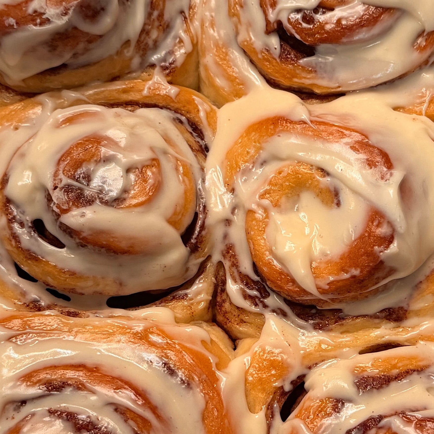 A tray of freshly baked cinnamon rolls with white icing, arranged in a silver aluminum pan.