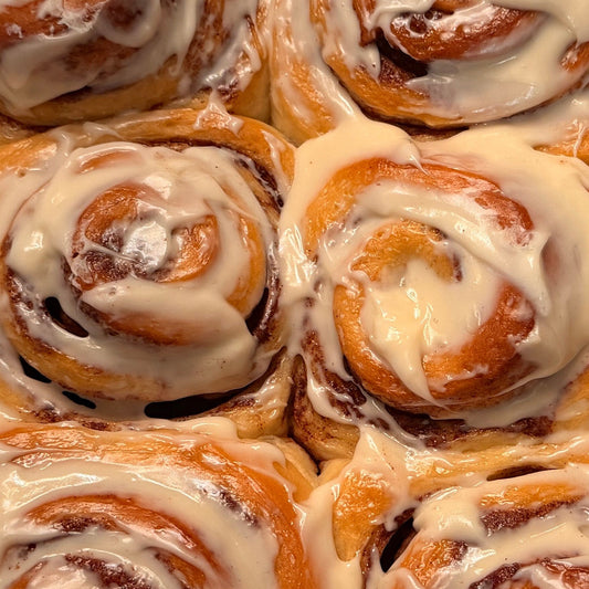 A tray of freshly baked cinnamon rolls with white icing, arranged in a silver aluminum pan.